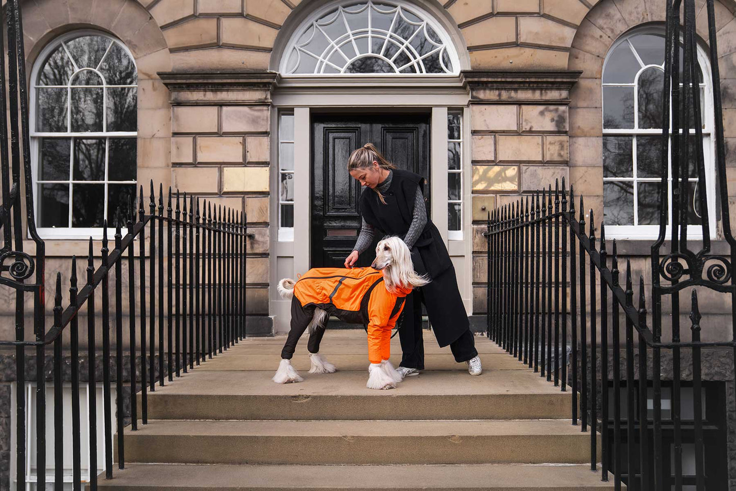 Chica ajustando un impermeable naranja non-stop dogwear en la ciudad en su galgo afgano