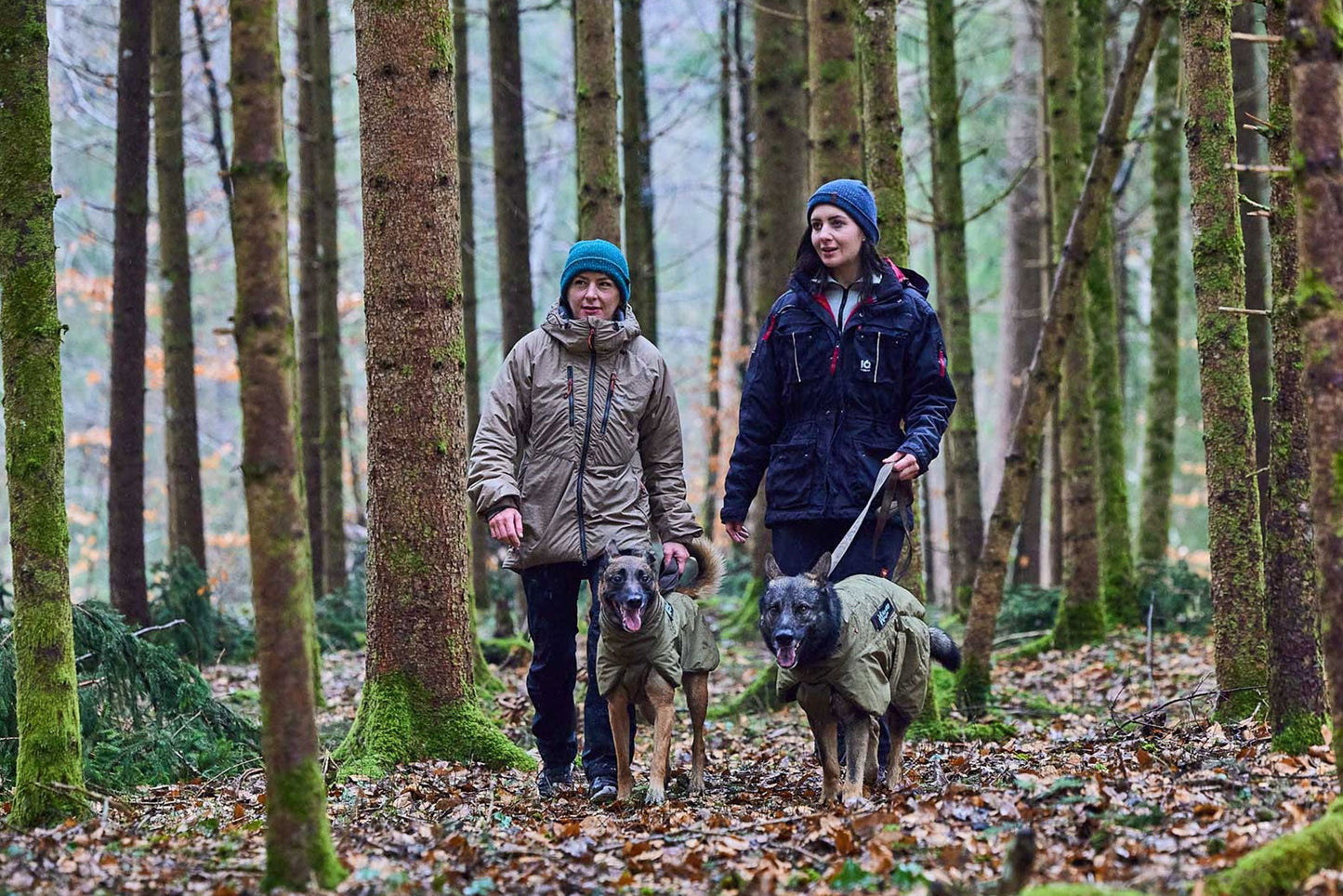 Dos chicas paseando con sus perros por el bosque con abrigo