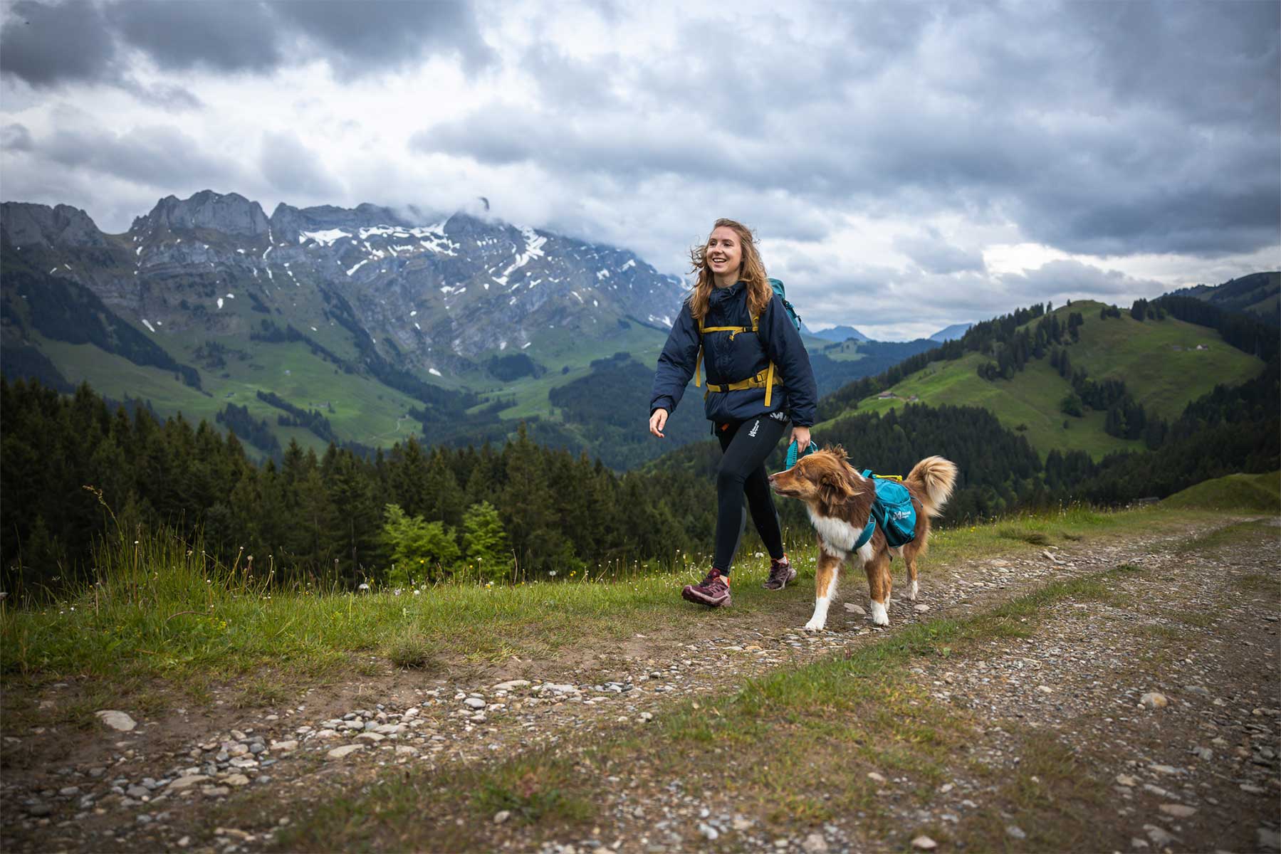 Chica paseando por la montaña con la mochila Non-stop dogwear Trail dog backpack y su perro
