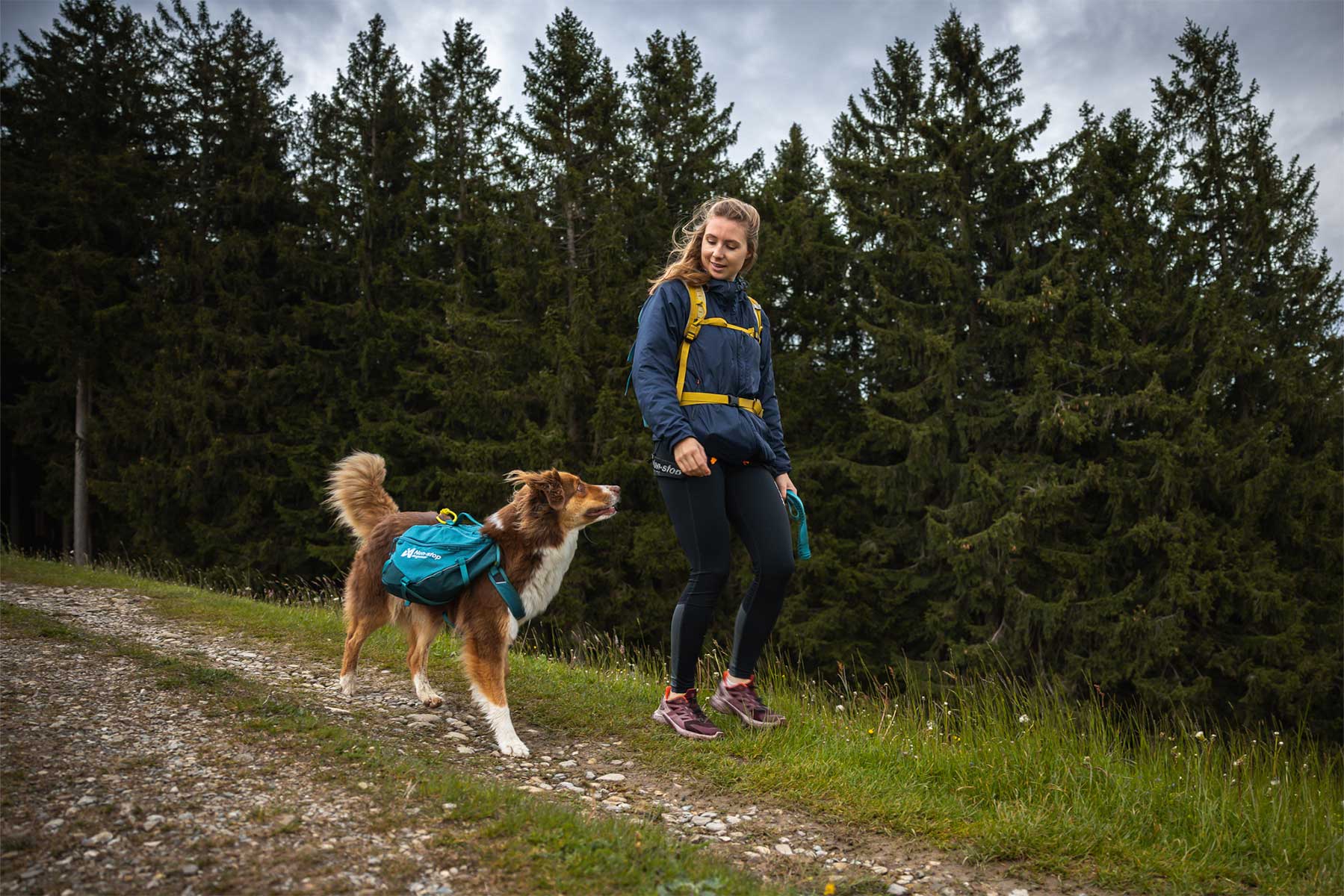 Chica paseando por el bosque con la mochila Non-stop dogwear Trail dog backpack y su perro